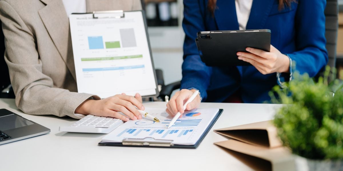 Two people in suits reviewing financial charts on clipboards.